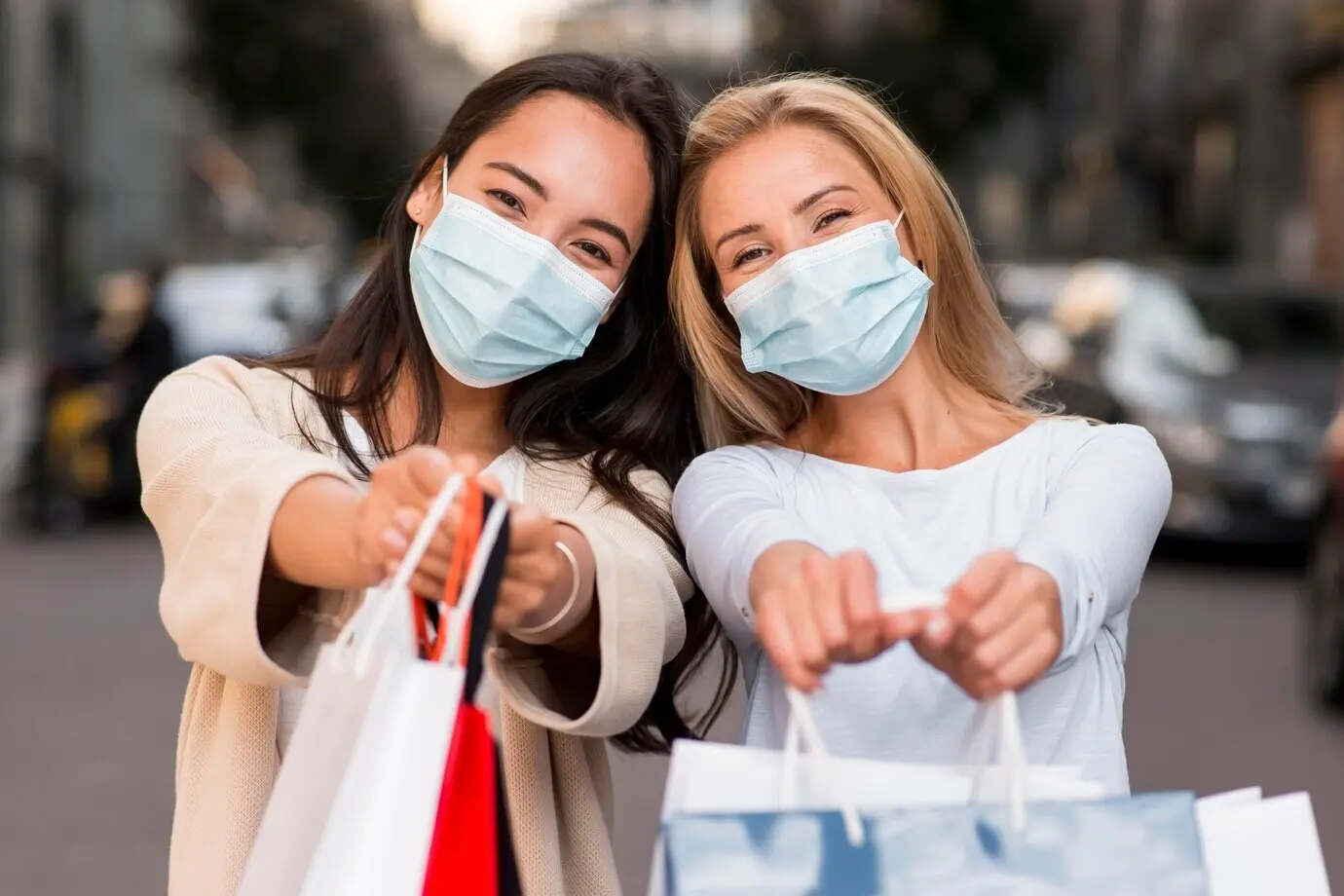 Deux femmes portant des masques médicaux posent ensemble avec des sacs de shopping.